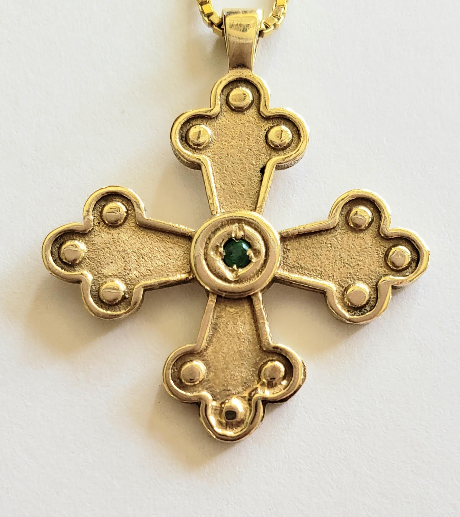 Gold cross pendant with a center gemstone on a white background