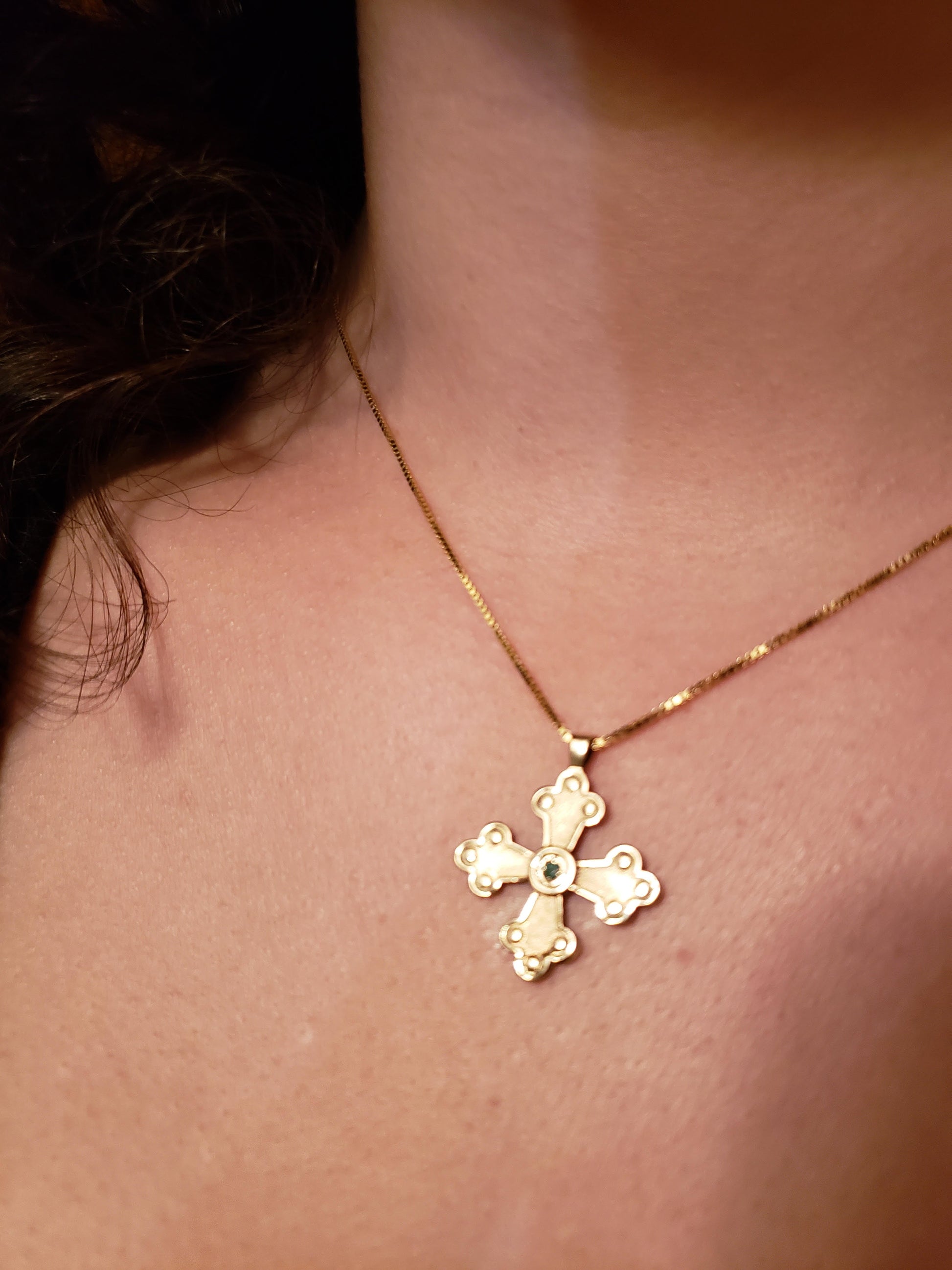 Woman wearing gold cross pendant with a center gemstone.