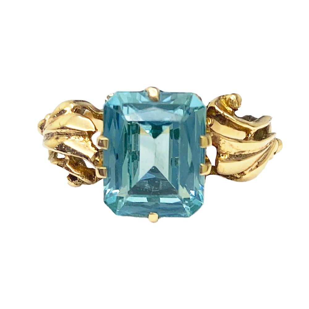 Gold ring with a large, emerald-cut green gemstone set in a delicate, floral-inspired setting.