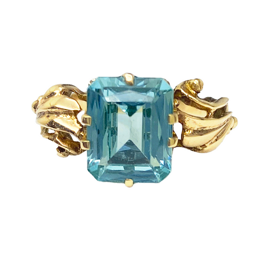 Gold ring with a large, emerald-cut green gemstone set in a delicate, floral-inspired setting.