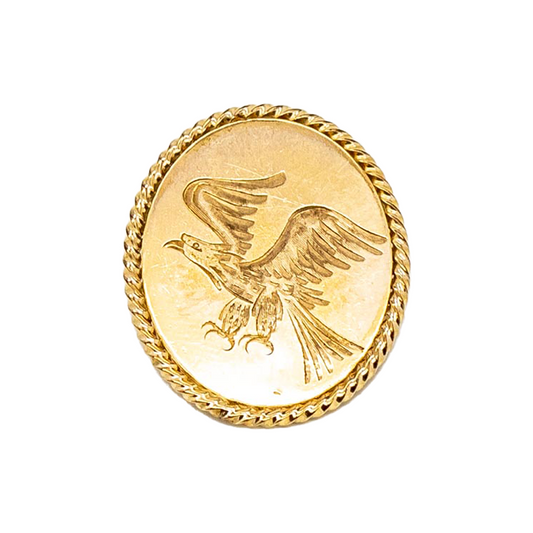 Circular gold pin featuring an engraved image of a soaring eagle with wings outstretched. 