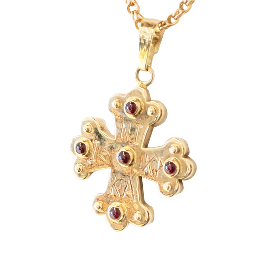 Gold cross pendant with a center gemstone on a white background