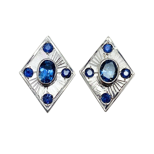 Silver earring features a central oval sapphire surrounded by six smaller sapphires, set in a geometric, diamond-shaped design.