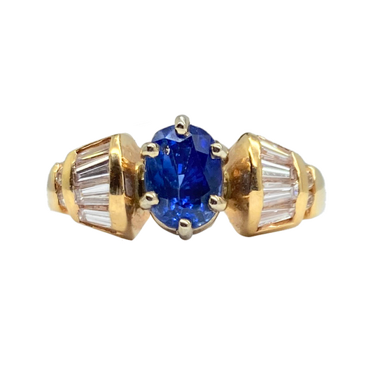 Gold ring featuring a central oval blue sapphire flanked by two rows of baguette-cut diamonds. 