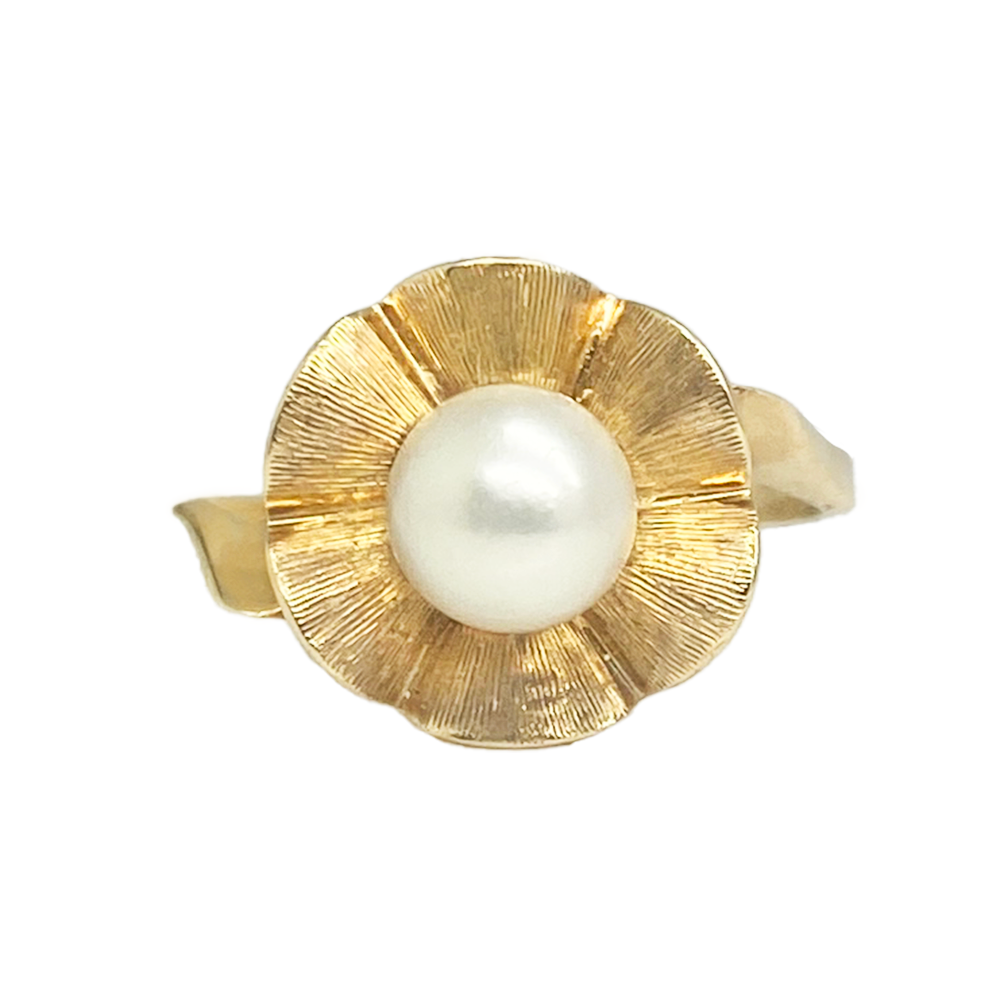 Gold ring featuring a round pearl set in a flower-shaped design with textured petals.