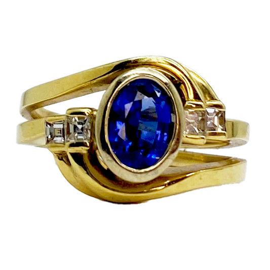 Gold ring featuring an oval sapphire set in a bezel, flanked by two square-cut diamonds.