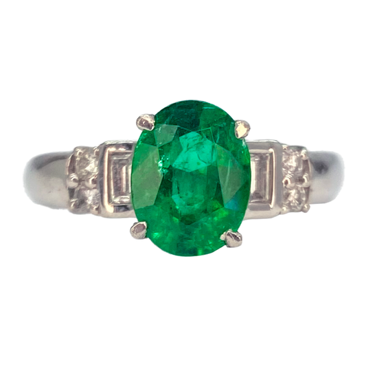 Silver ring featuring an oval emerald, flanked by two trapezoid-cut diamonds.