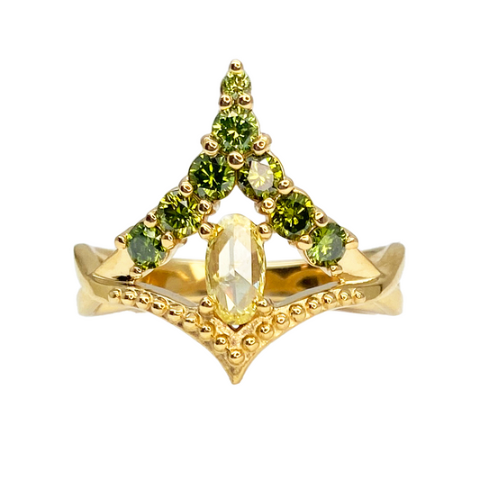 Yellow gold ring featuring a central oval diamond flanked by two rows of green gemstones in a triangular setting. 