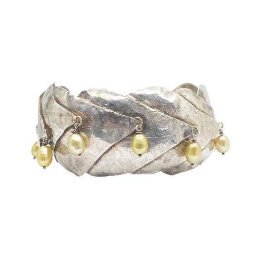 Silver cuff bracelet with multiple dangling yellow pearls.