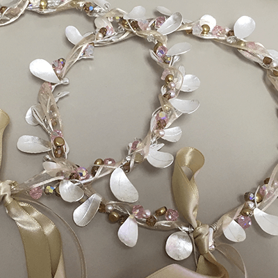 Pair of delicate, leaf-shaped hair crowns adorned with pink and white pearls, silver beads, and gold accents. The crowns are tied together with a gold ribbon.