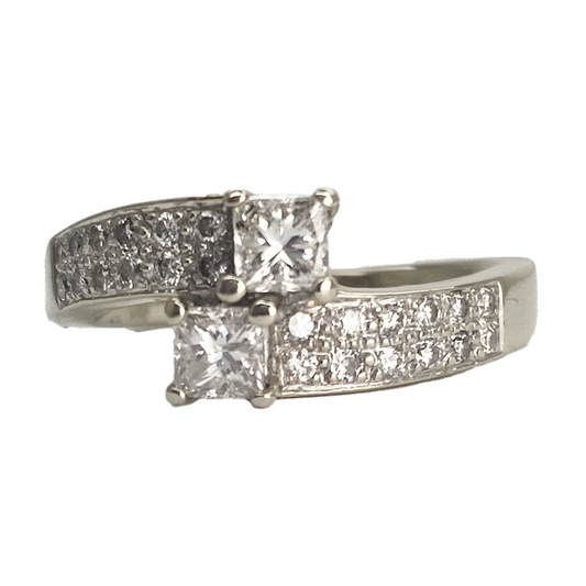 Twisted silver ring featuring two princess-cut diamonds, each surrounded by a halo of smaller diamonds.