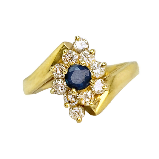 Gold ring featuring a central blue sapphire surrounded by a cluster of round diamonds. 