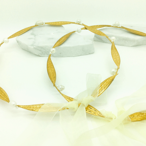 Pair of gold wedding crowns adorned with olive leaves and pearls, tied together with a white ribbon.