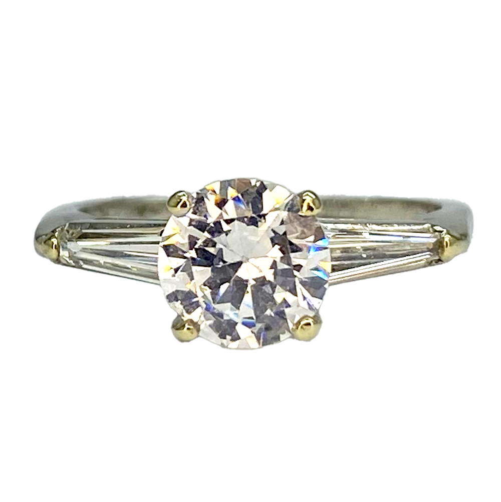 Vintage Cartier diamond ring with a round center stone flanked by baguette side stones, set in a silver band with a gold bezel.