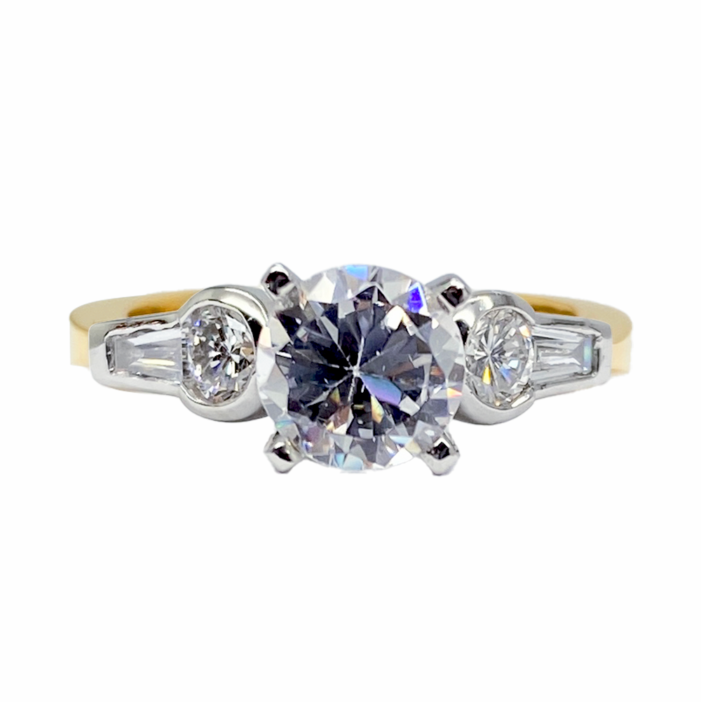 Three-stone diamond engagement ring with a round center stone flanked by baguette side stones.