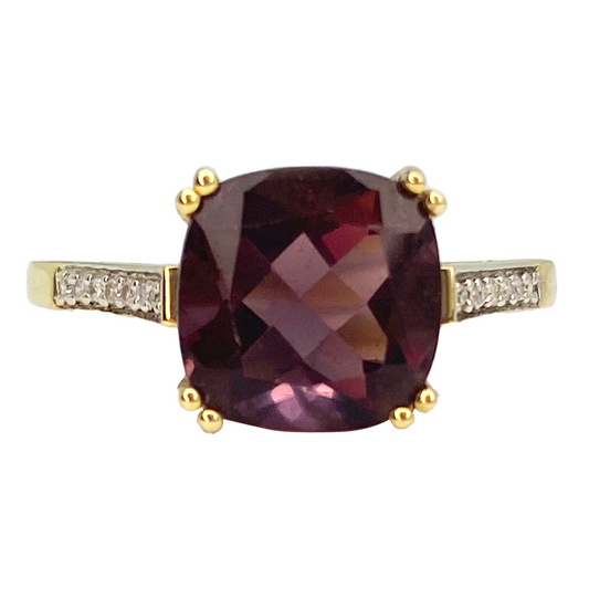 Cushion-cut purple gemstone ring with a gold setting and diamond accents on the band.