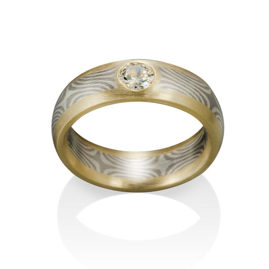 Two-tone gold ring with a round diamond and a Damascus steel band on a white background