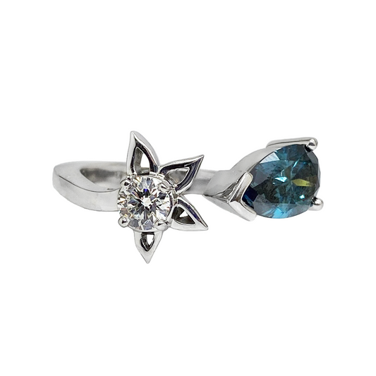 Silver ring featuring a split shank design with a delicate flower motif on one side and a pear-shaped blue gemstone on the other.