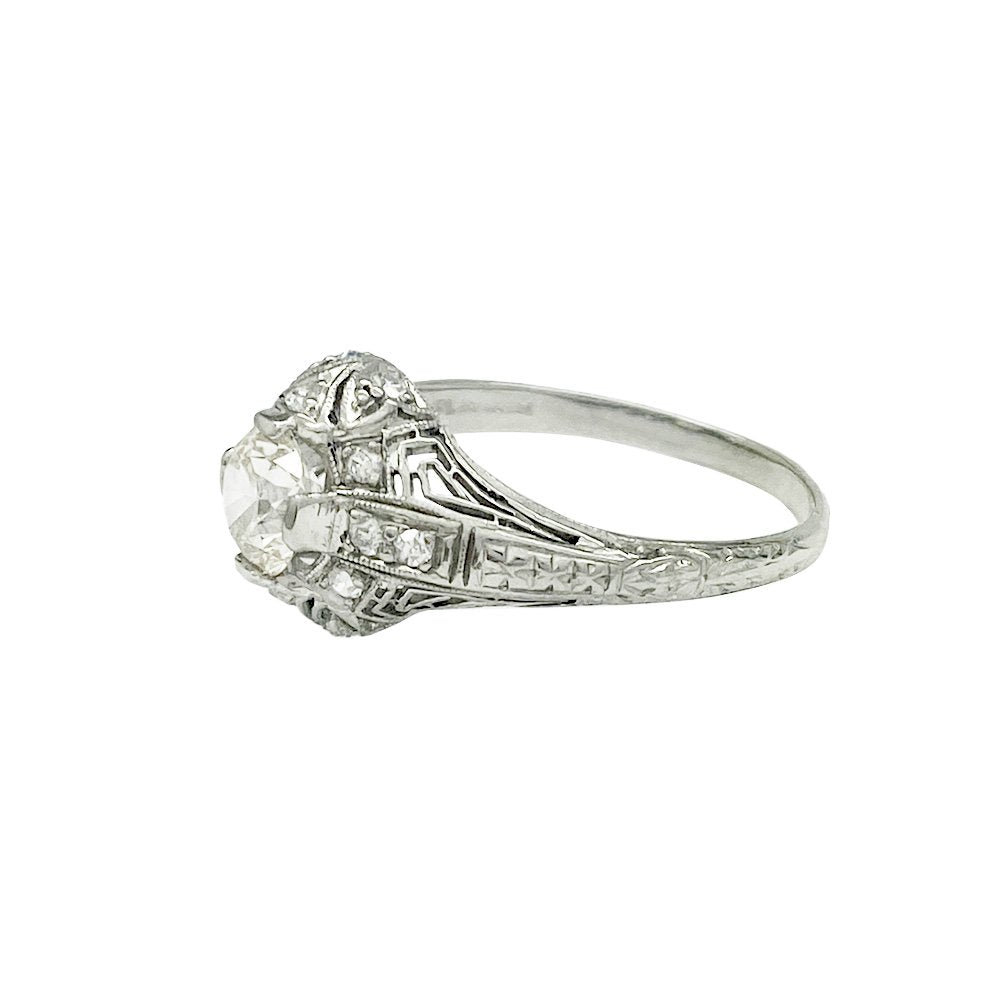 Silver diamond ring with a central round diamond surrounded by smaller diamonds in a geometric setting.