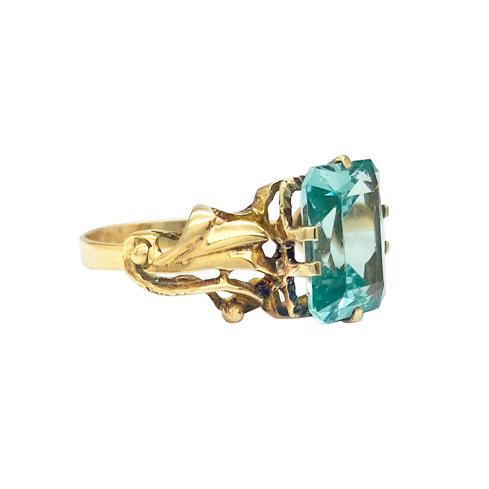 Gold ring with a large, emerald-cut green gemstone set in a delicate, floral-inspired setting.