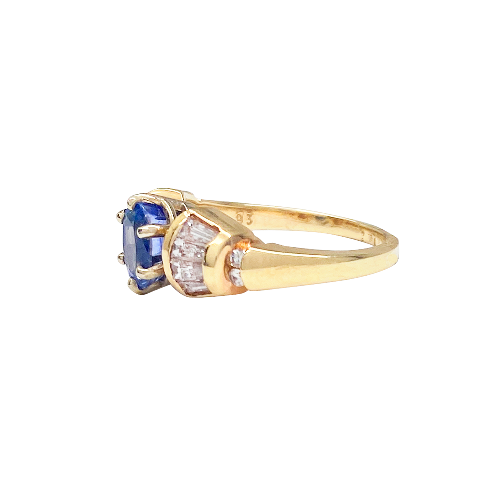 Gold ring featuring an oval-cut sapphire surrounded by baguette-cut diamonds.