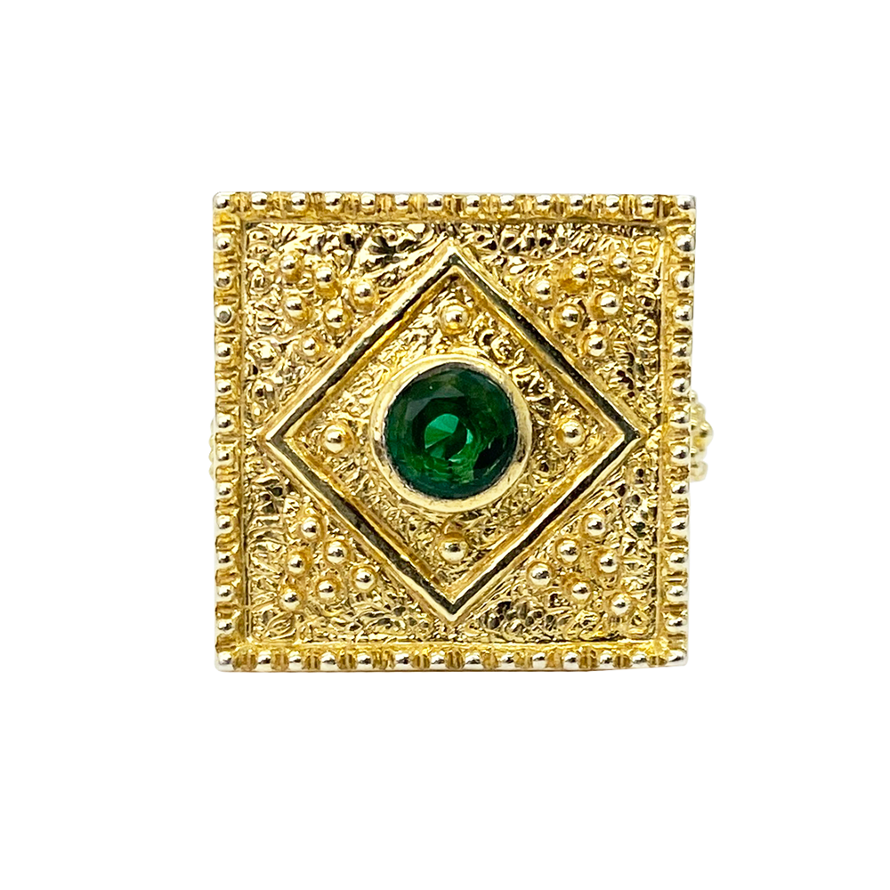 Gold ring with a square setting featuring an emerald center stone and intricate textured details, on a white background.