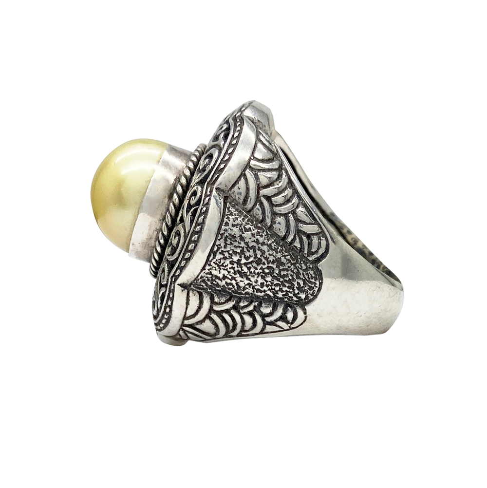 Silver ring with a large, round pearl set in an intricate, textured design, on a white background.