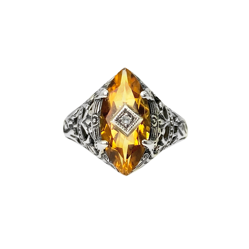 Silver ring with a yellow citrine center stone and intricate filigree detailing, on a white background.