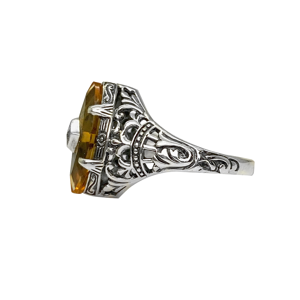 Silver ring with a yellow citrine center stone and intricate filigree detailing, on a white background.