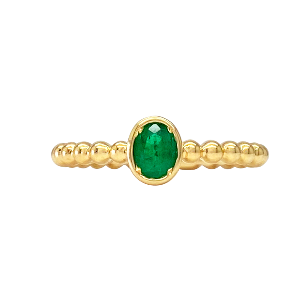 Oval emerald ring with a beaded gold band on a white background