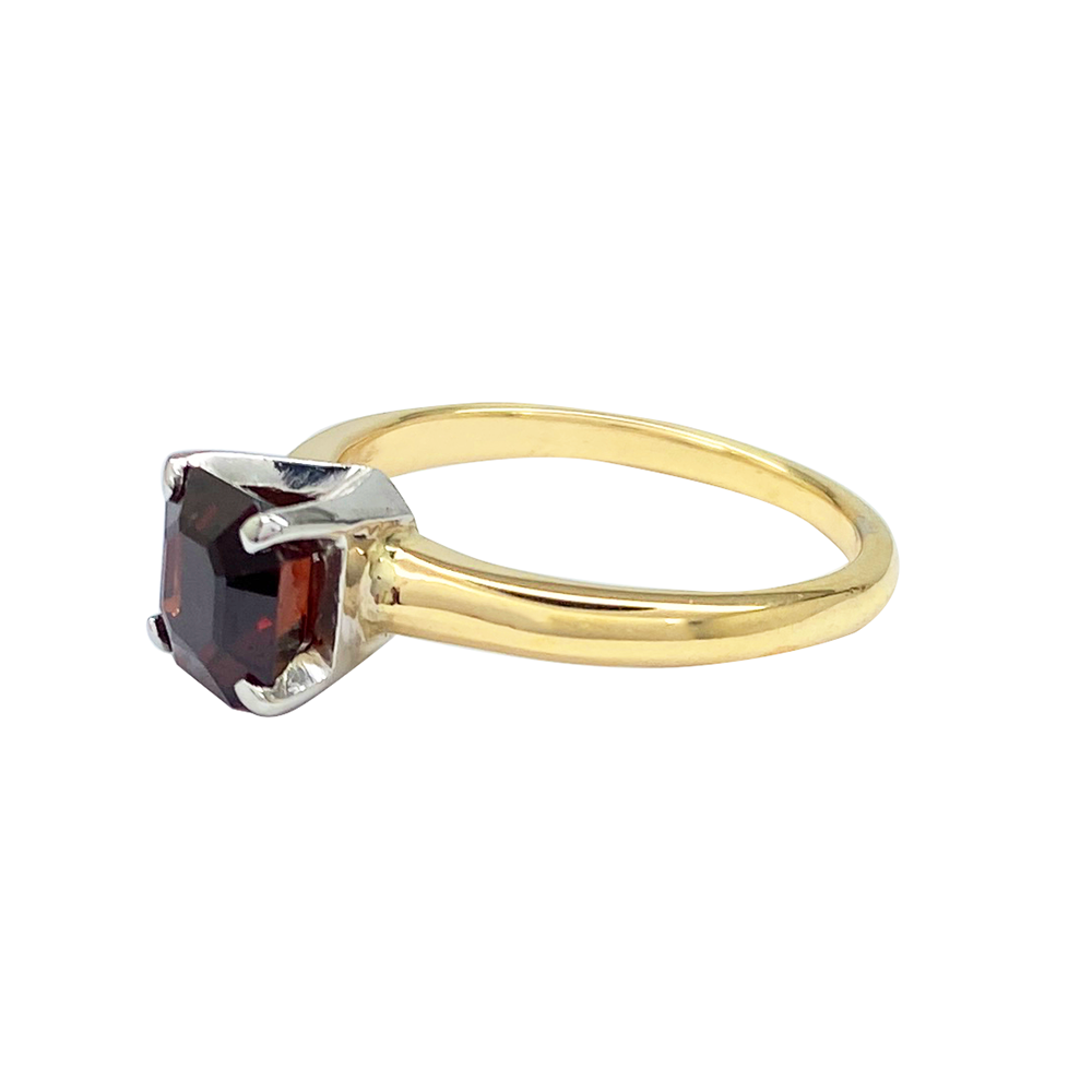 Yellow gold ring with an asscher-cut garnet center stone on a white background.