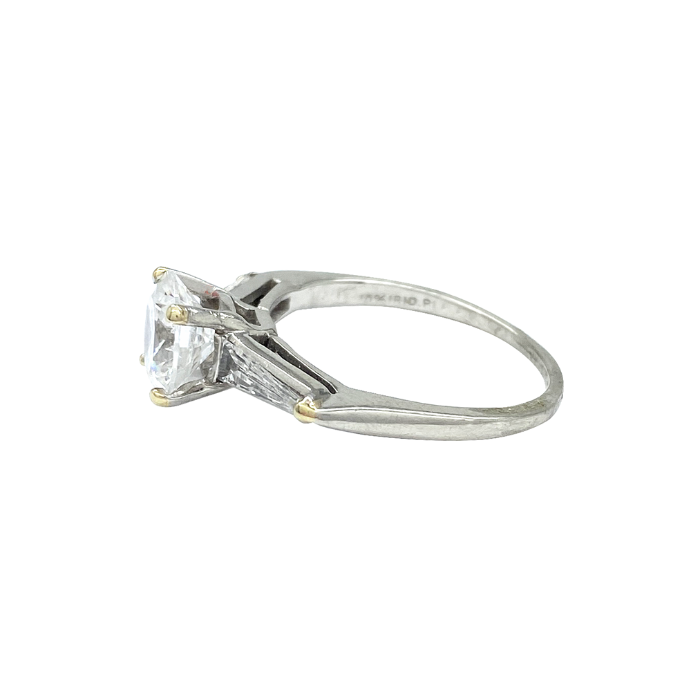 SIlver engagement ring with a round diamond center stone and baguette-cut side stones, on a white background.