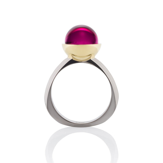 Ring with a large, round, red gemstone set in a gold bezel, on a white background.