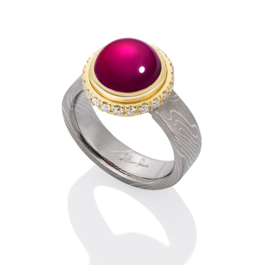 Ring with a large, round, red gemstone set in a gold bezel, on a white background.