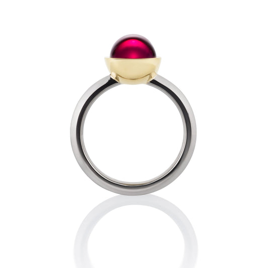 Ring with a large, round, red gemstone set in a gold bezel, on a white background.