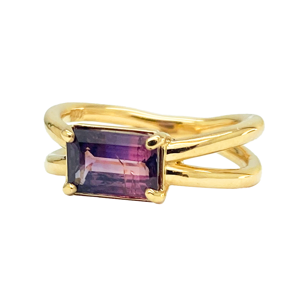  Gold ring with a rectangular, purple gemstone set in a split shank band on a white background.