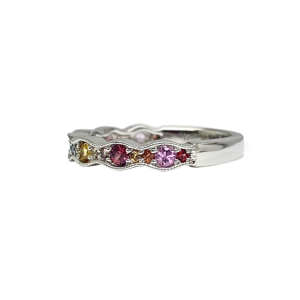 Side view of silver multi-gemstone ring with a wavy band featuring round sapphires in various colors including pink, purple, blue, yellow, and orange. 